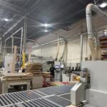 Wide view down the cabinet factory floor with overhead dust collection, roller conveyor and stacked cut parts | Sunshine Alliance, Deerfield Beach FL