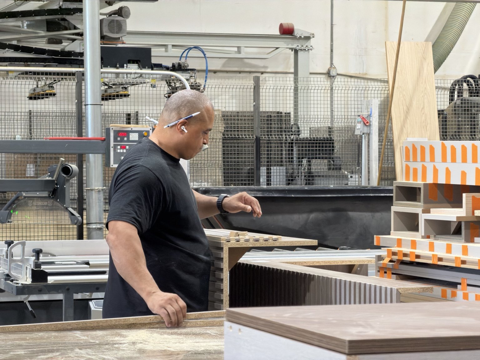 Craftsman handling a stack of melamine-faced panels at the edgebander, banded cabinet boxes stacked alongside | Sunshine Alliance, Deerfield Beach FL