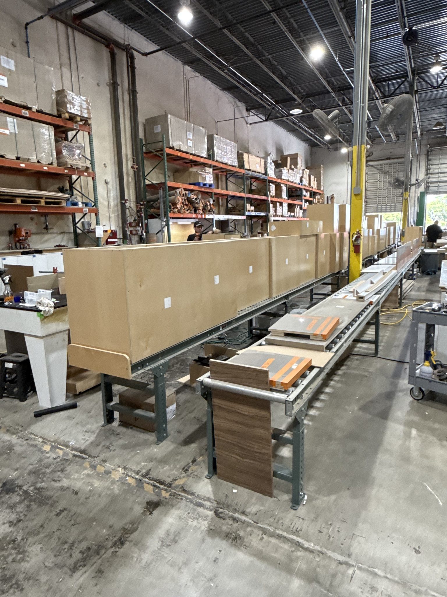 A long custom cabinet run staged on the conveyor beside cut panels and edged parts | Sunshine Alliance, Deerfield Beach FL